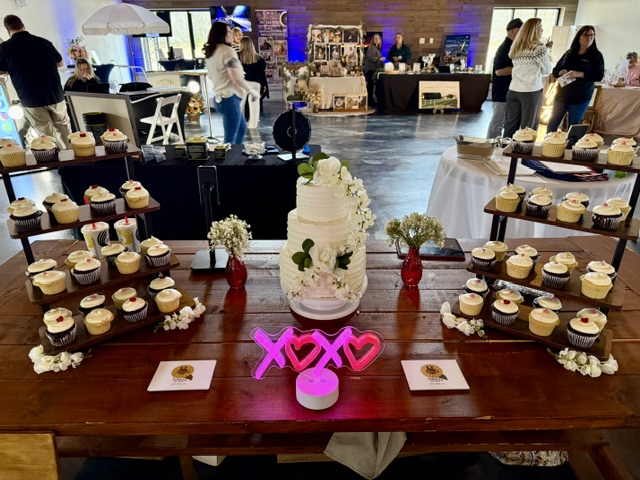 Wedding cake and cupcake display with floral accents and XOXO neon sign